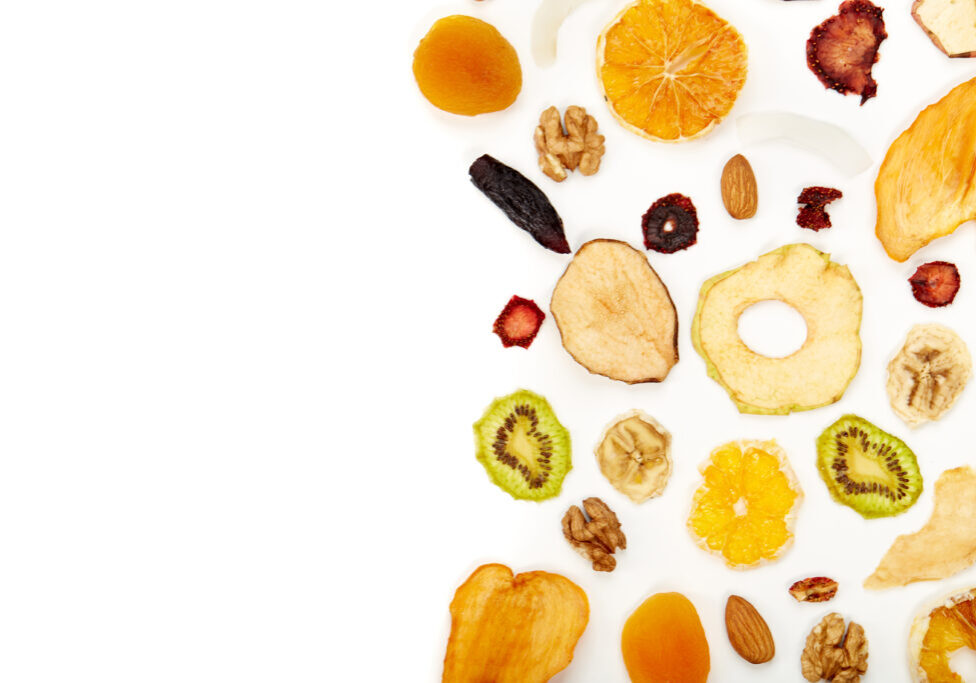 Above view of neatly stacked dried fruit different colors and almonds, orange, dried apricot, raisins, walnuts, dried apples and kiwi on white background. Concept of healthy snacks.