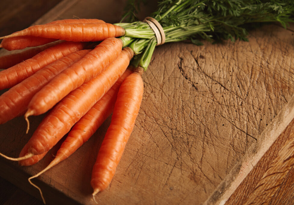 Close up shot of a bunch of fresh ripe carrots on an old chopping board with deep cuts