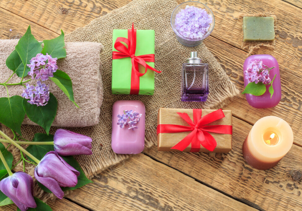 Terry towels, soap and sea salt for bathroom procedures, a burning candle, gift boxes, a bottle of perfume and tulip flowers on sackcloth and old wooden boards. Top view. Spa products and accessories.