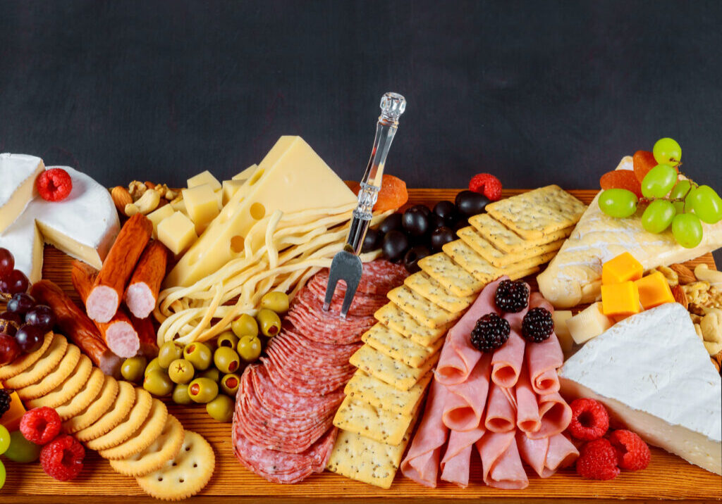 Beautiful decor of fresh cheese and meat crackers, green olives, nuts and berries on wooden gray boards