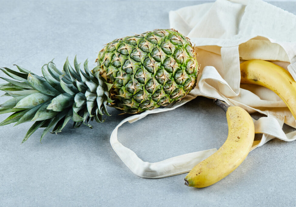 Ripe pineapple and banana in a white bag on blue background. High quality photo