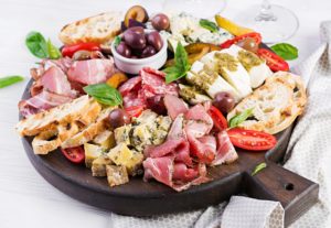 Antipasto platter with ham, prosciutto, salami, blue cheese, mozzarella with pesto and olives on a wooden background.